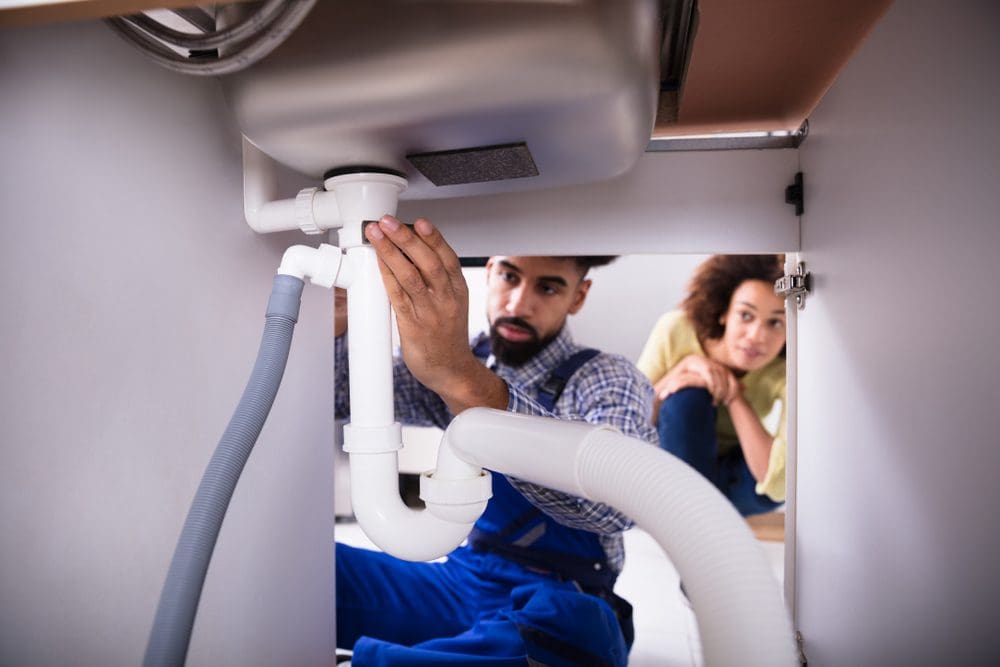 plumber taking a look under sink at drain for drain cleaning